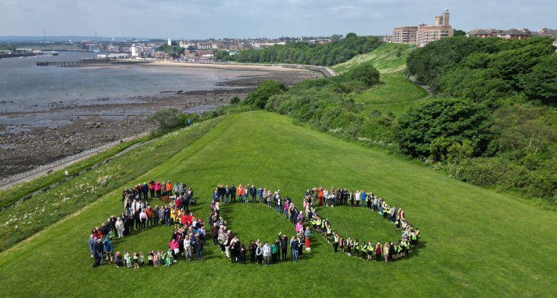 a large group of people standing on the headland overlooking North Shields in the shape of an 800