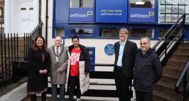 A group of five people standing in front of the Charles Minto blue plaque