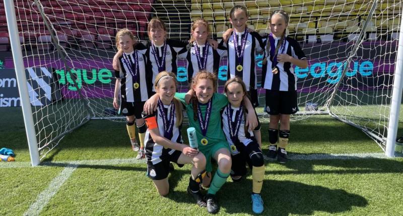 The winning team pictured in the goal, holding their trophy and medals. 